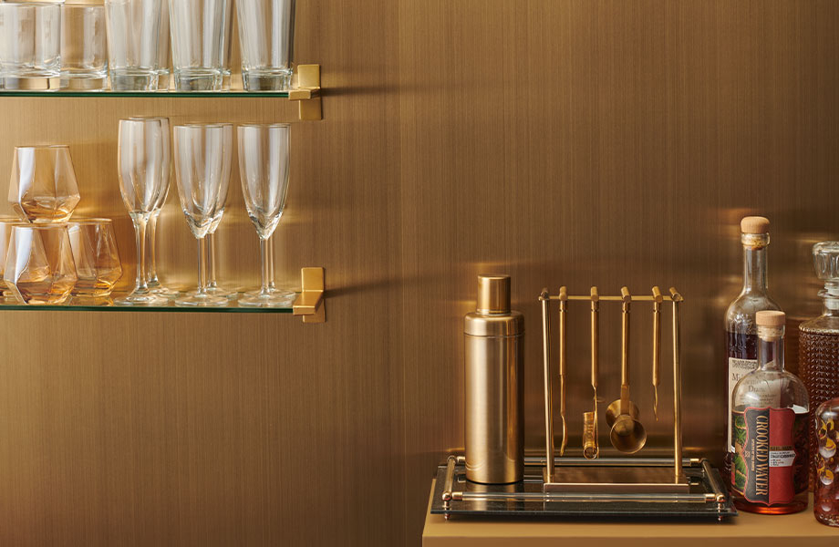 Barware, bottles and glassware set against a Wax Rubbed Brass Homapal Metal Laminate accent wall 