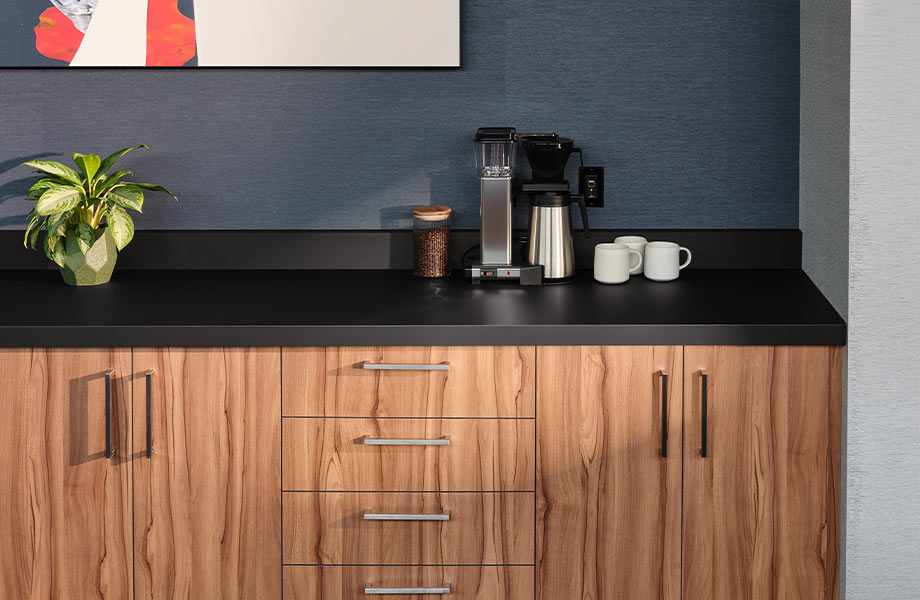Coffee station in a breakroom featuring woodgrained cabinets and a black countertop