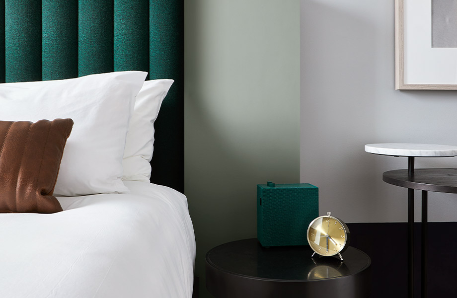 Chambre d'hôtel avec literie de couleur blanche, tête de lit vert foncé, table de chevet avec horloge et mur accent en couleur J0794 Verde Kitami des matériaux FENIX